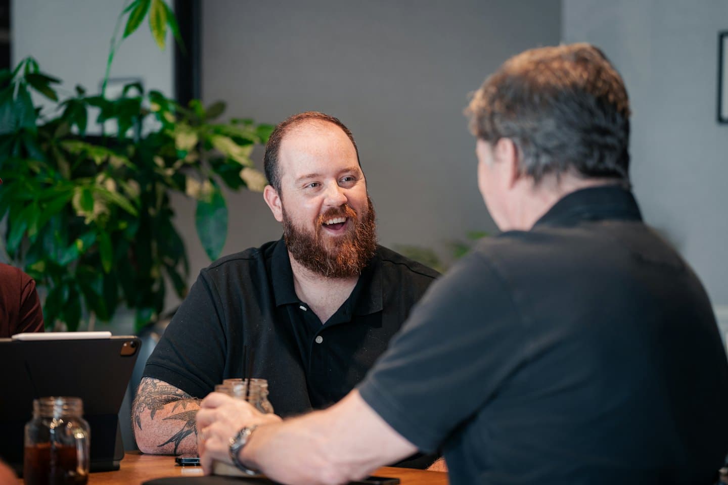 Two men discuss business over drinks and a tablet.