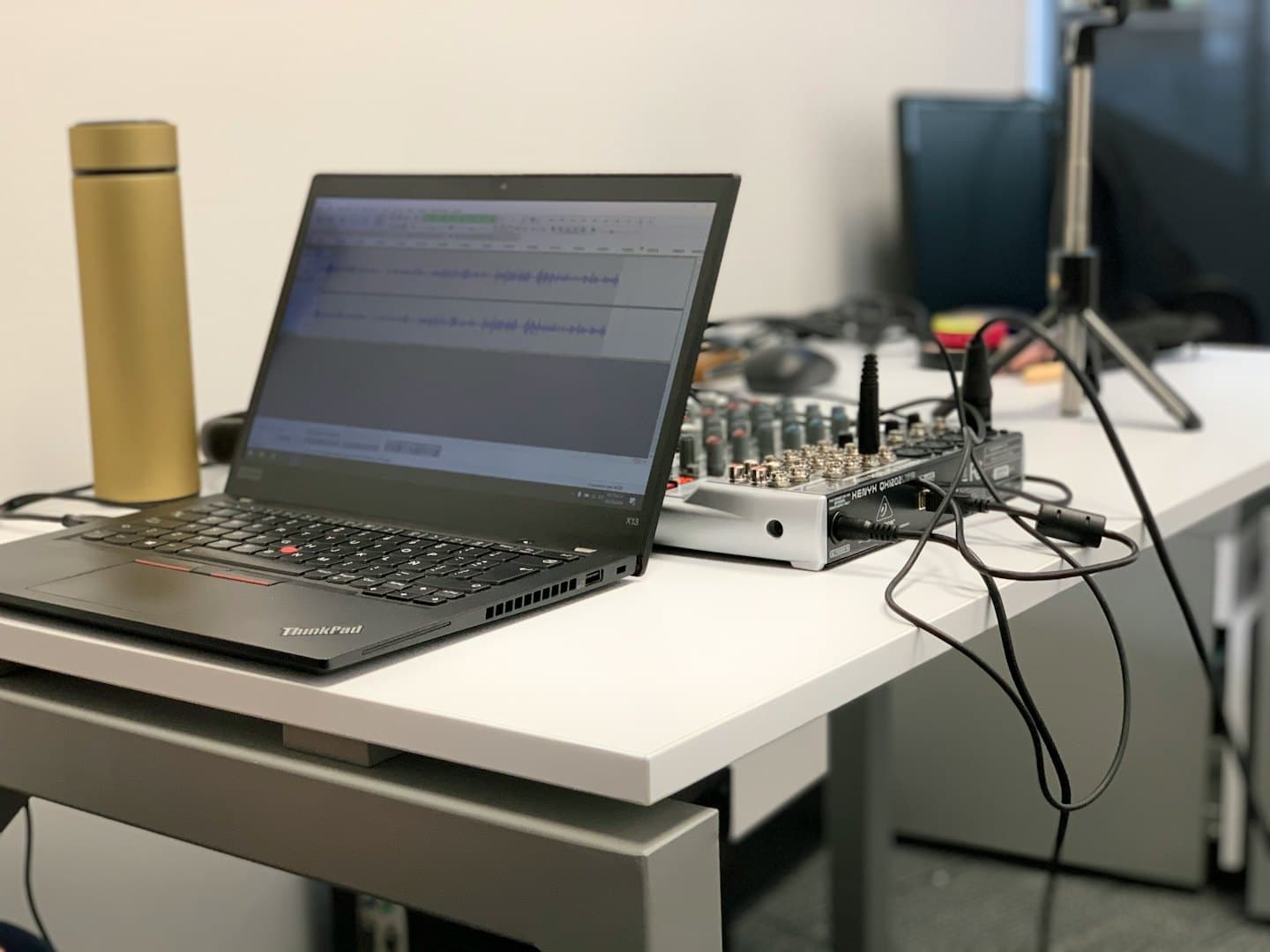 Laptop with audio mixer and water bottle on desk.
